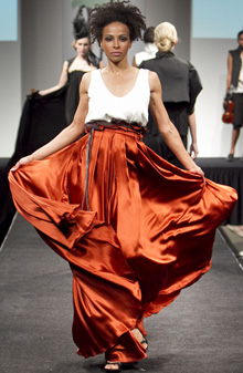 Model on runway with white and orange flowing gown on